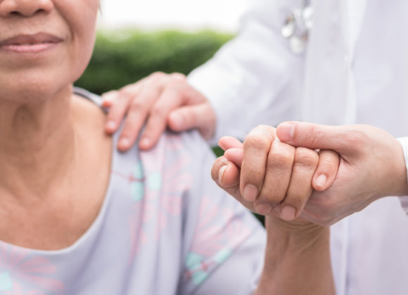 Elderly senior dementia patient (aging old adult person) in nursing hospice home holding geriatrician doctor's hand having happy medical health care from hospital carer or caregiver healthcare service